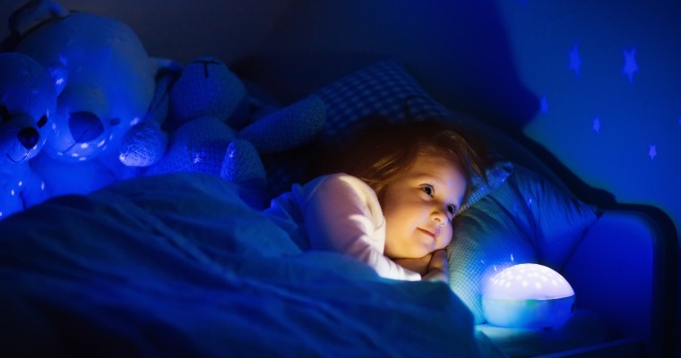 Muzyczny projektor gwiazdek pomaga w zaśnięciu leżącej w łóżku dziewczynce